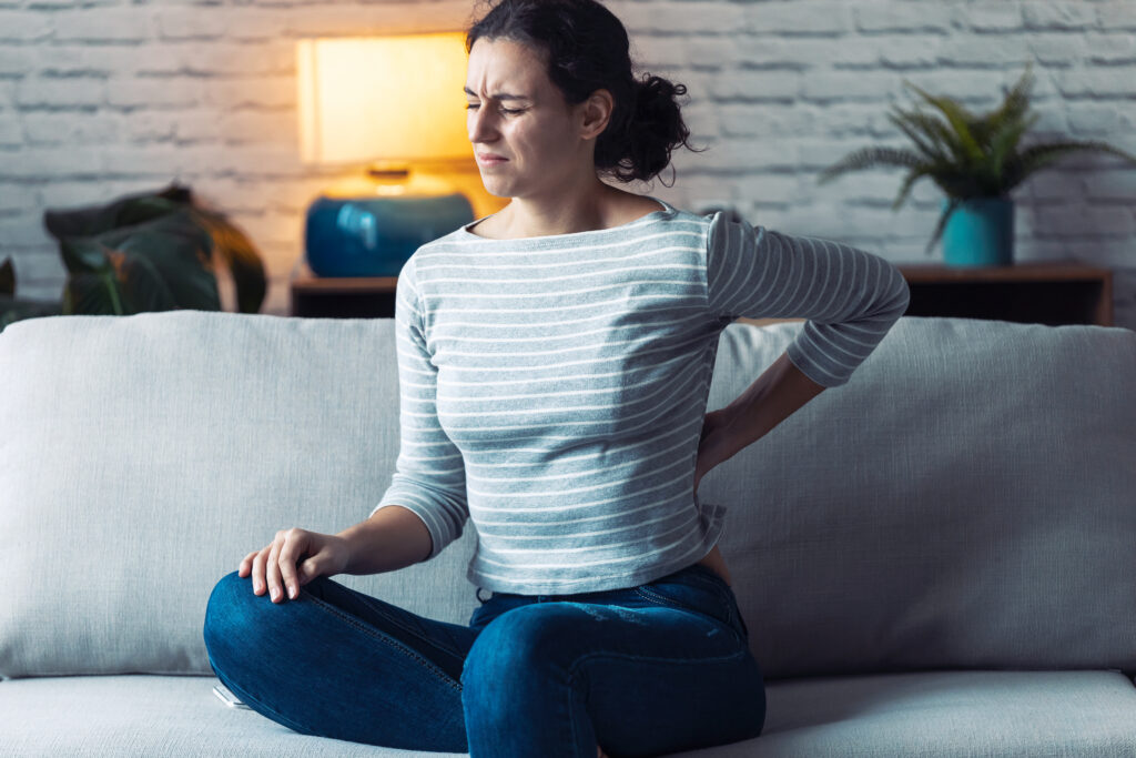 woman sitting on couch suffering from back pain and needs to see a burnaby bowen therapy clinic